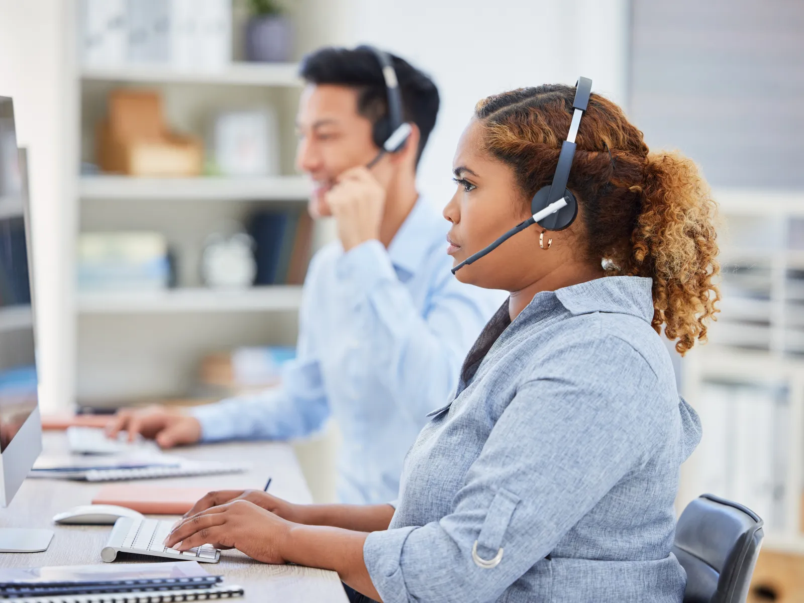 Focused customer service representatives wearing headsets working at computers in a bright office environment.