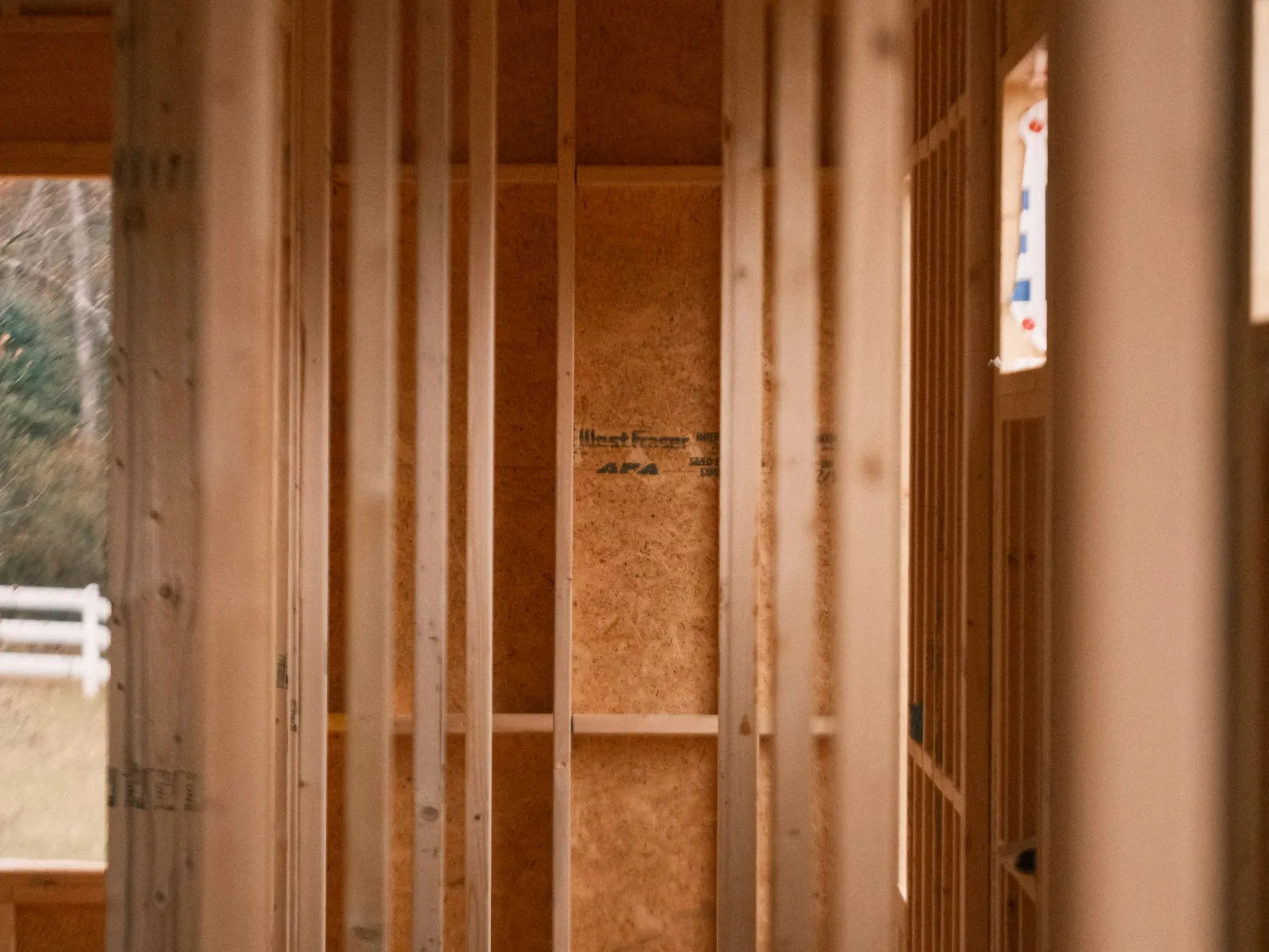 Interior view of a wooden house under construction showing framed walls and natural light.