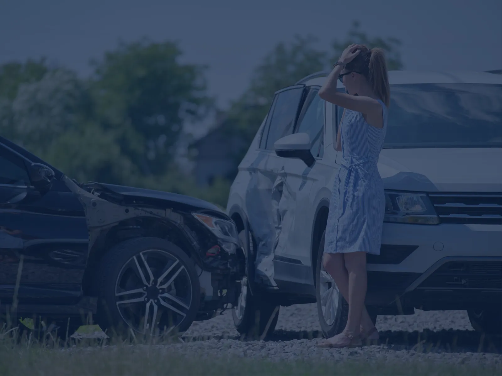 Woman in blue dress stands by two damaged cars after a roadside collision on a sunny day