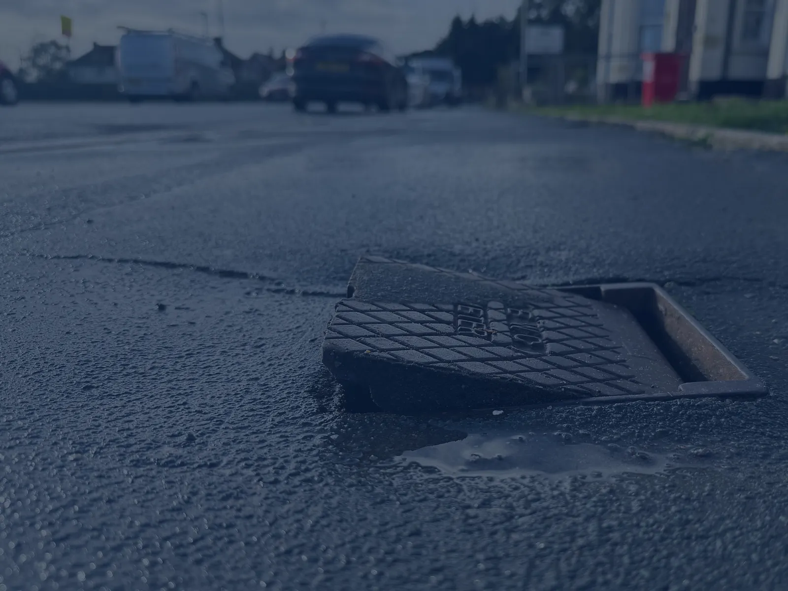 Close-up of a broken manhole cover on an asphalt street with blurred vehicles in the background.