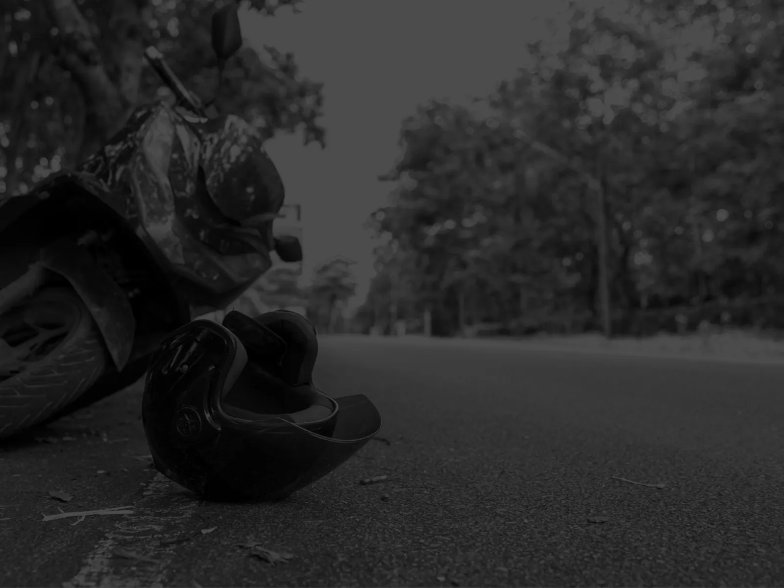 Motorcycle helmet lying on road beside a parked motorcycle with trees in the background under daylight.