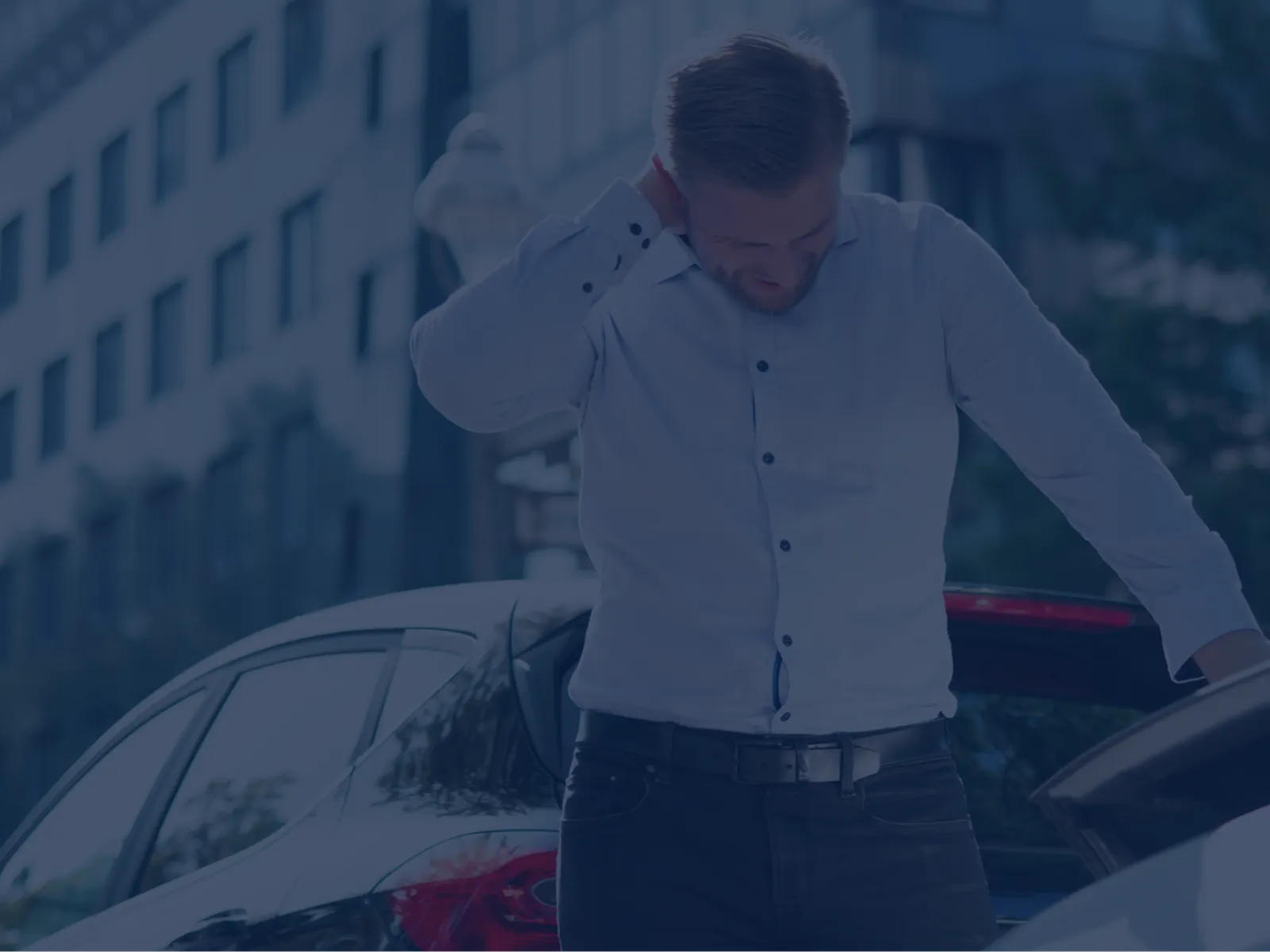 Man in white shirt inspecting car trunk in urban setting with office buildings in the background.