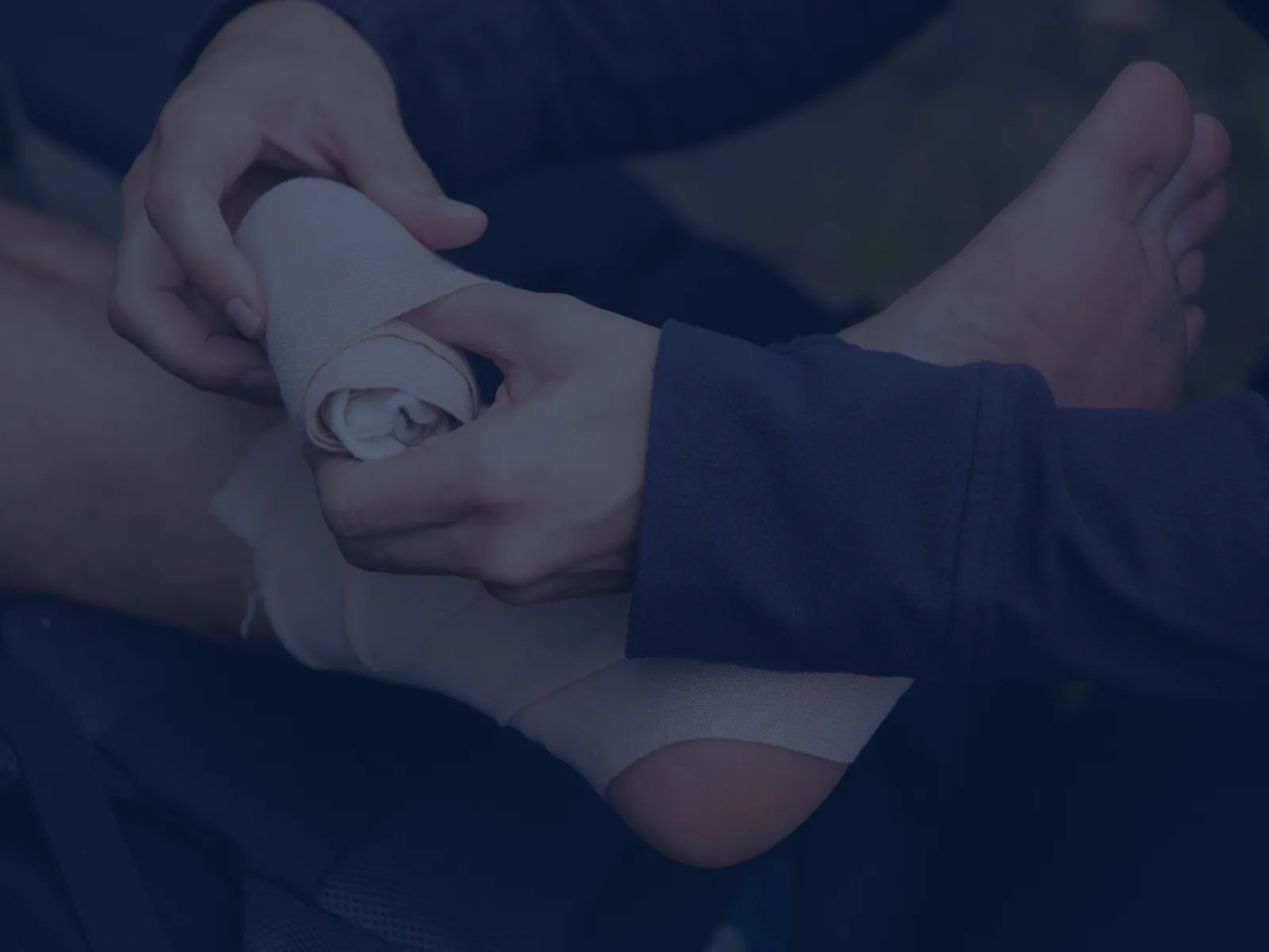 Person wrapping an ankle with a beige elastic bandage for support or injury care outdoors.
