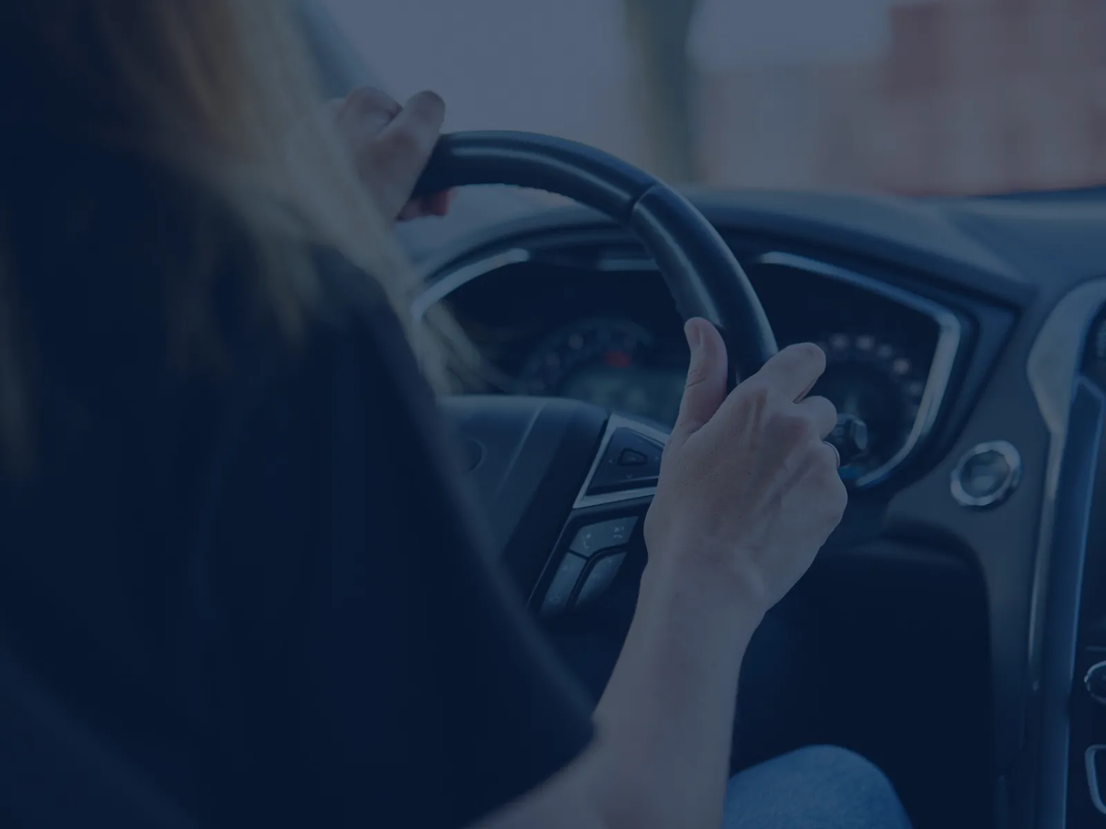 Close-up of a person’s hands gripping a car steering wheel while driving, dashboard and controls visible
