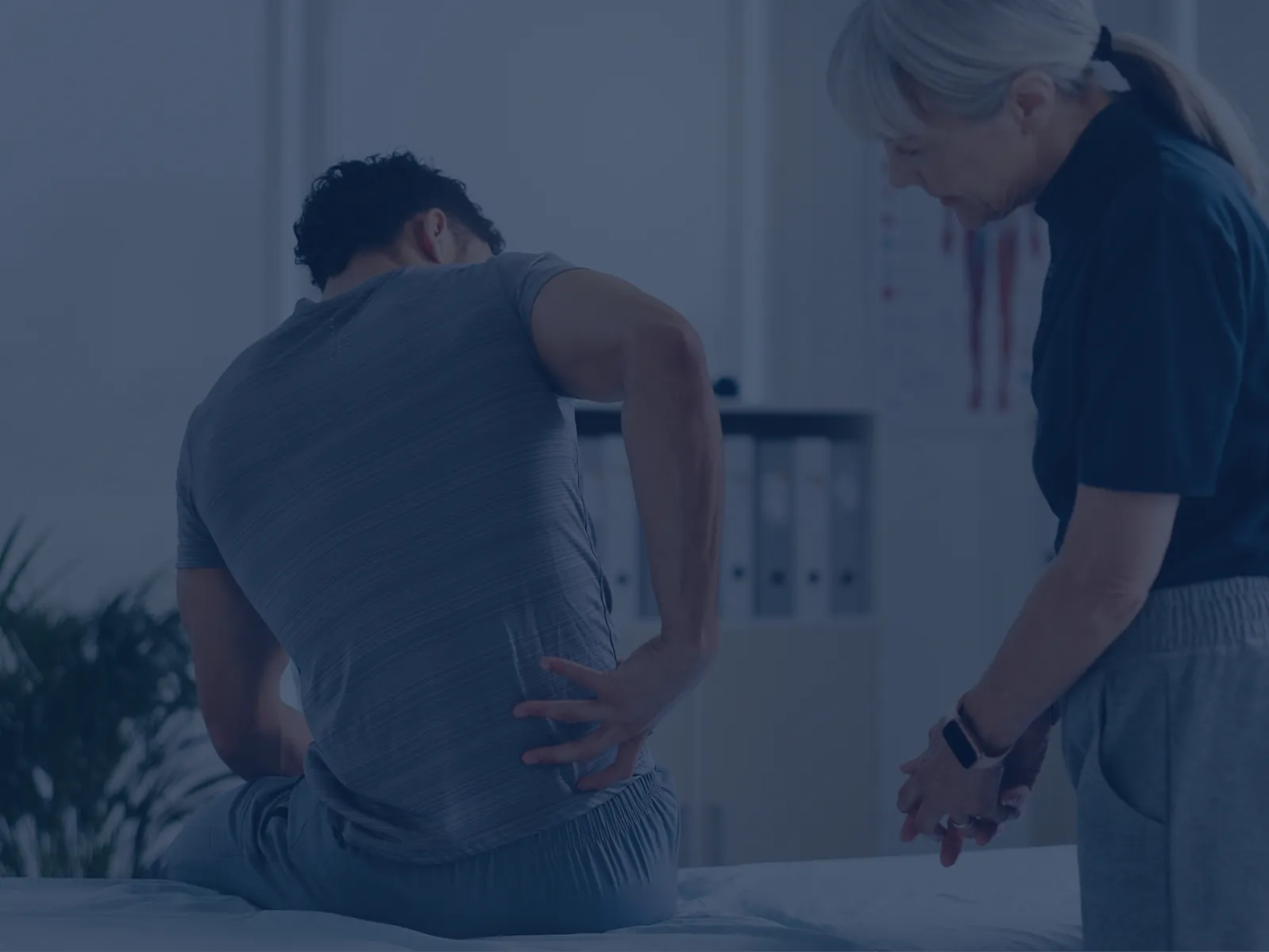 Therapist assisting man with back pain in a clinical setting, focusing on physical rehabilitation and care.