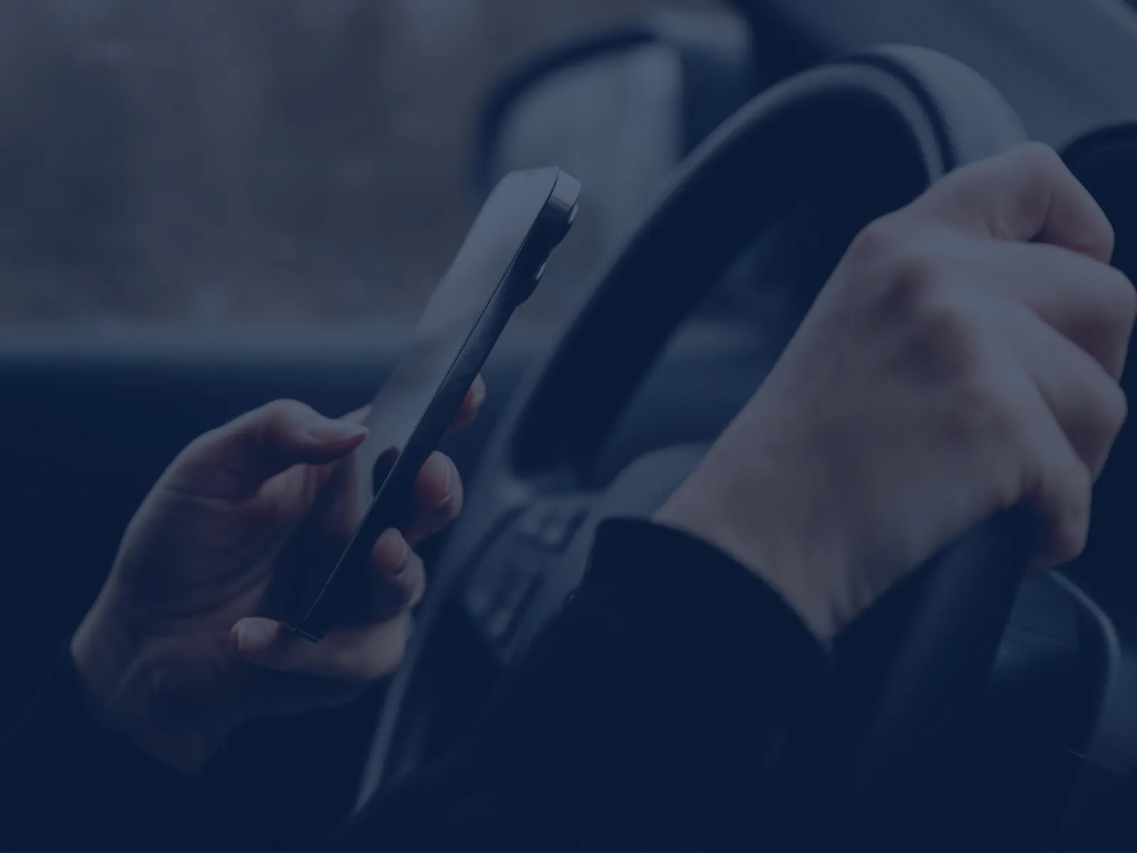 Person holding a smartphone in one hand and steering wheel with the other inside a car