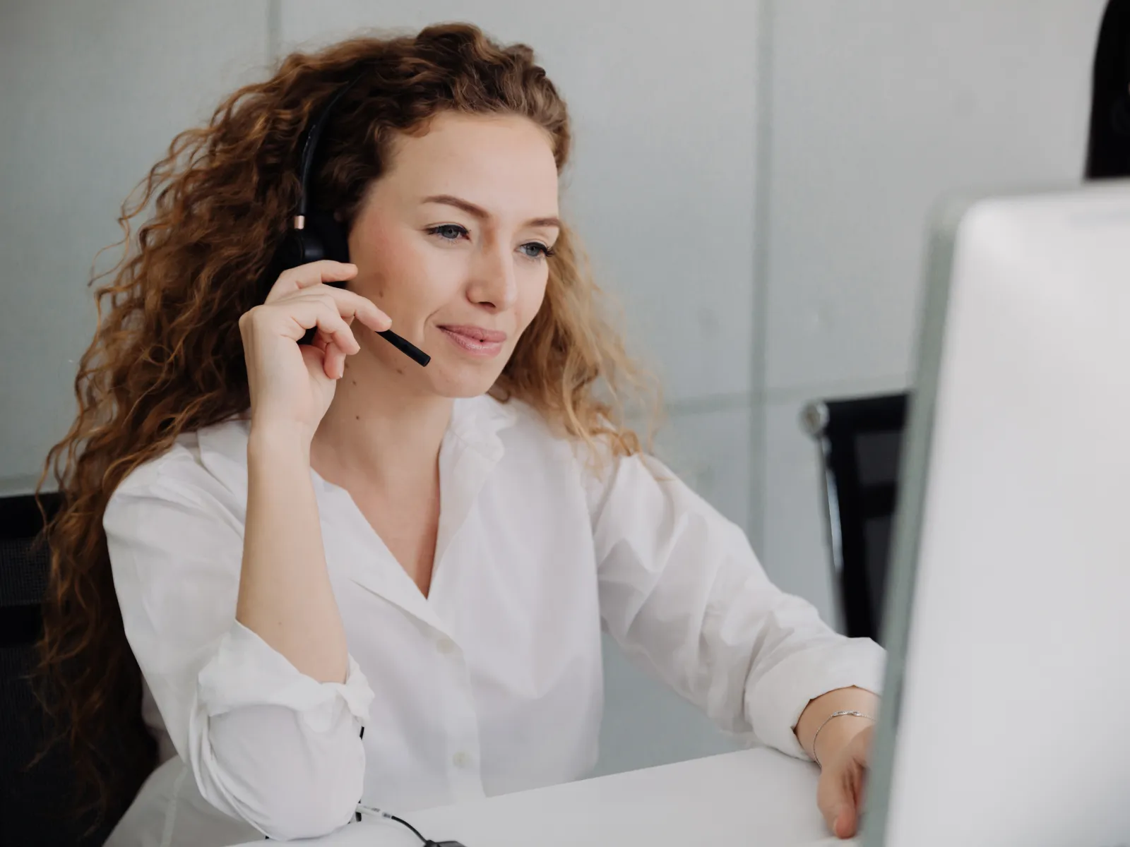 Smiling female customer service representative wearing headset working at computer in modern office