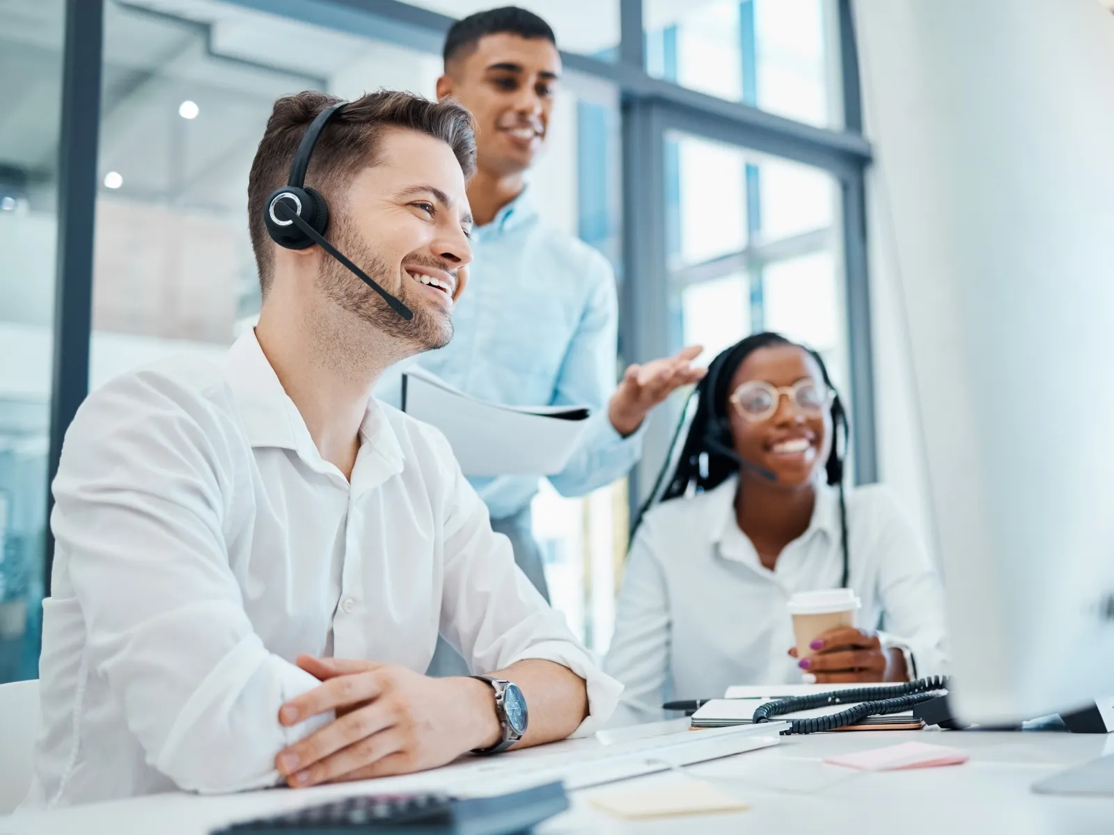 Smiling customer service team wearing headsets working together at a computer in a bright modern office.