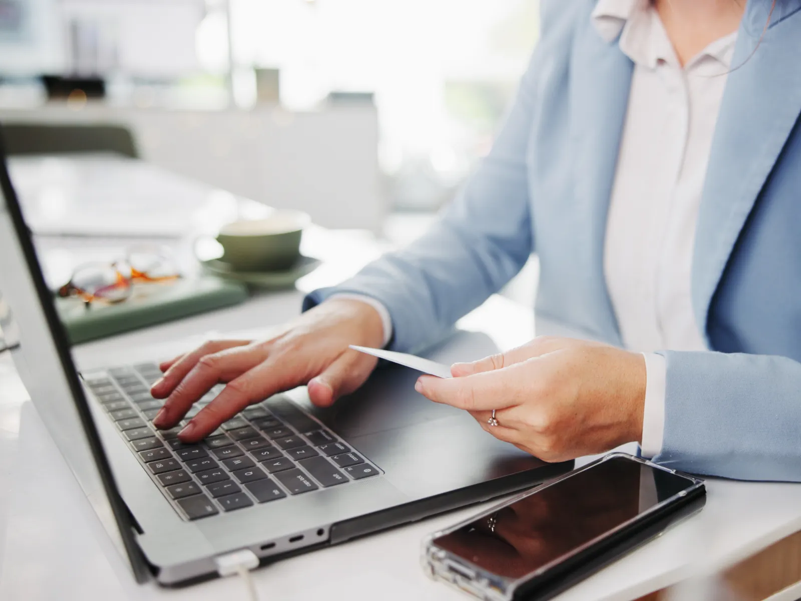Businesswoman using laptop and holding credit card for online transaction at office desk with smartphone