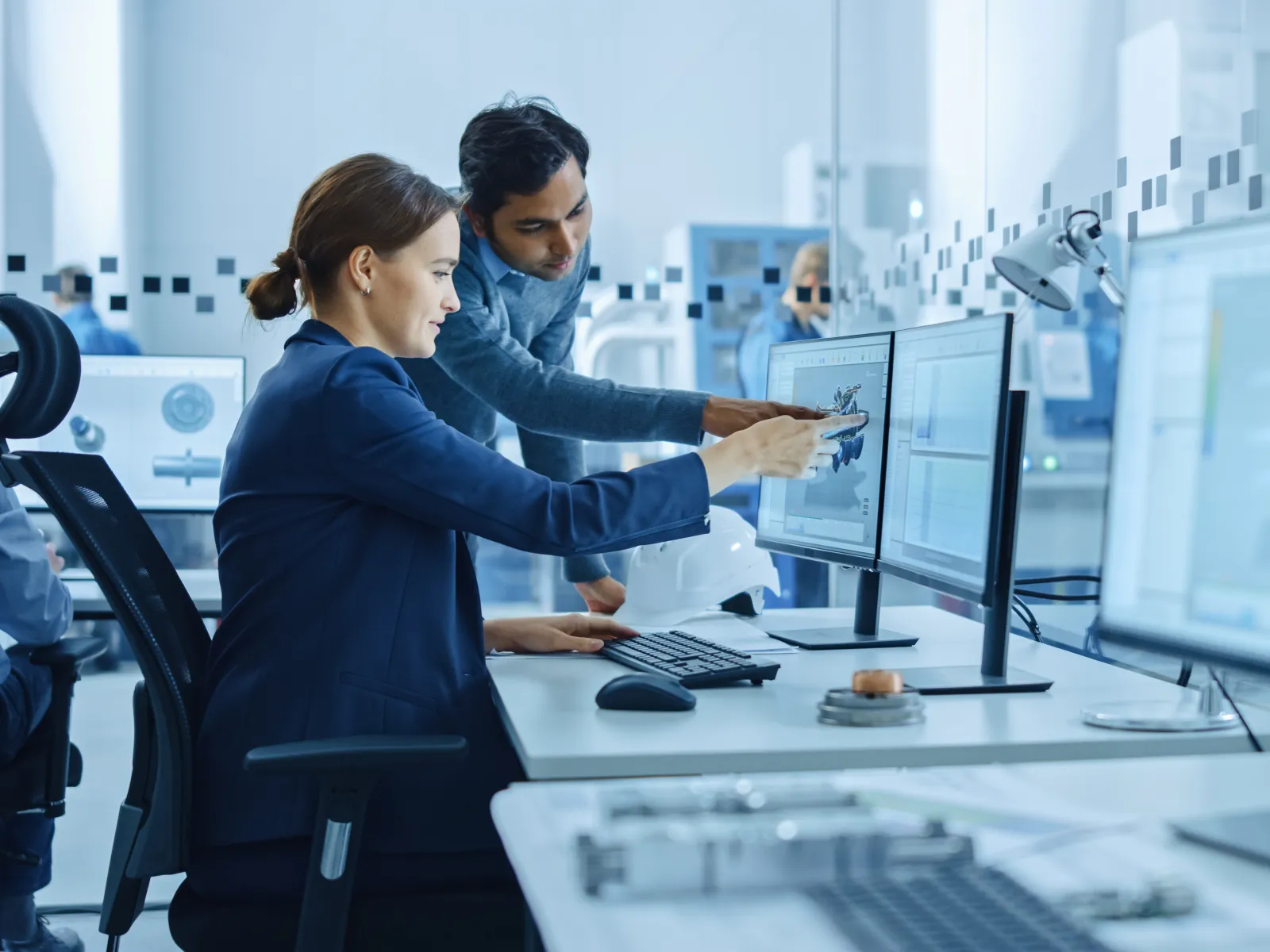 Two engineers analyzing 3D mechanical design on dual monitors in a modern office with CAD software.