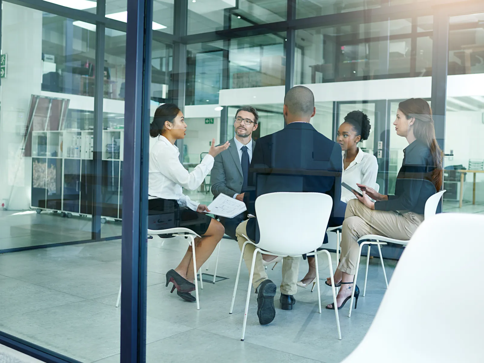 Group of diverse professionals having a meeting in a modern glass office, discussing business ideas.