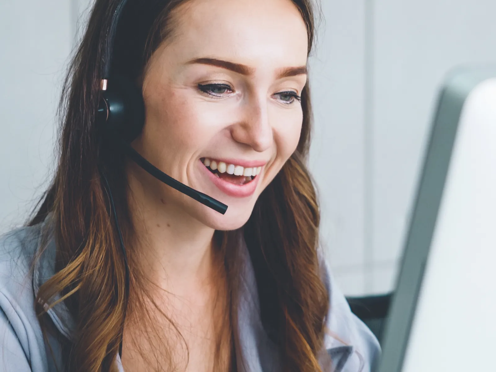 Smiling woman with headset working on computer providing customer support in modern office environment