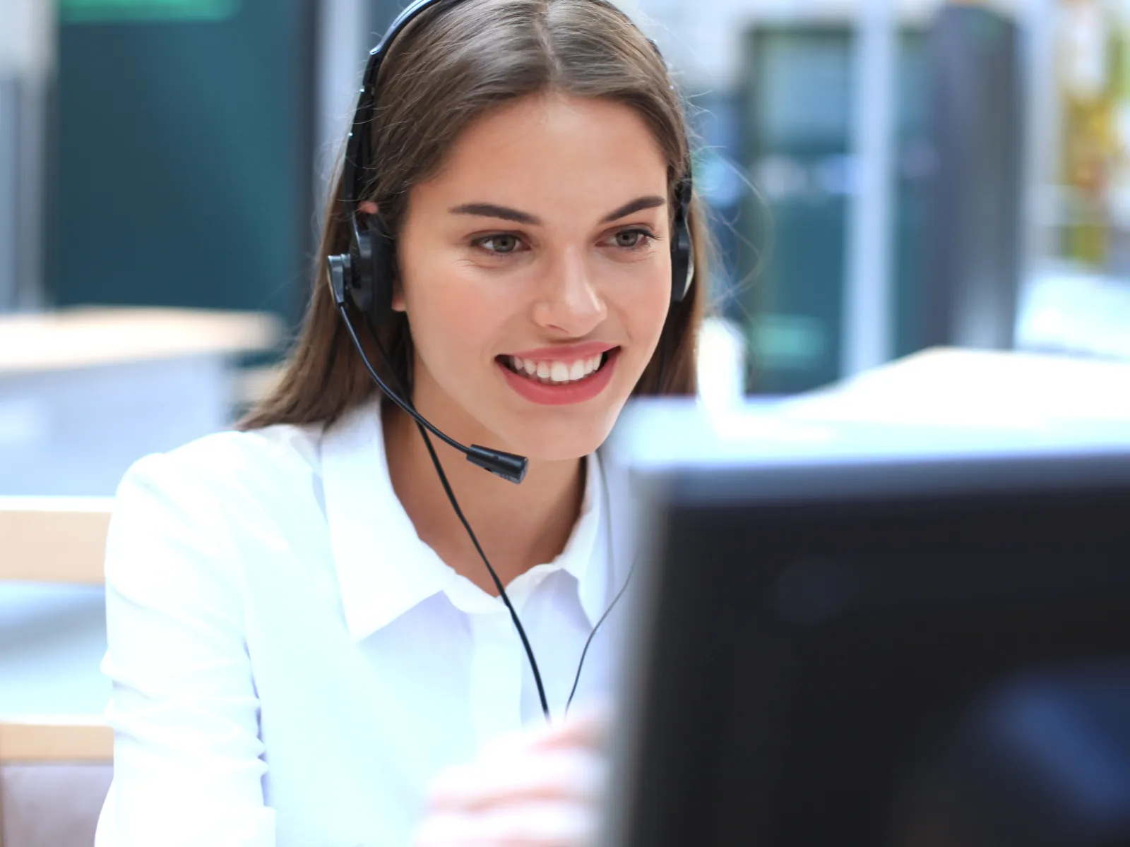 Smiling woman wearing headset working as customer service representative at computer in office environment.