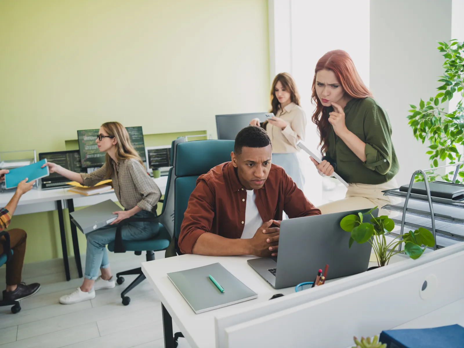 Diverse team collaborating in a modern office with laptops, documents, and focused expressions.