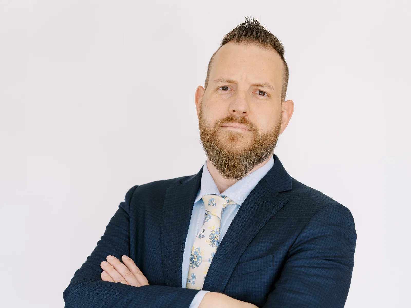 Confident business professional in a navy suit with arms crossed, standing against a plain background.