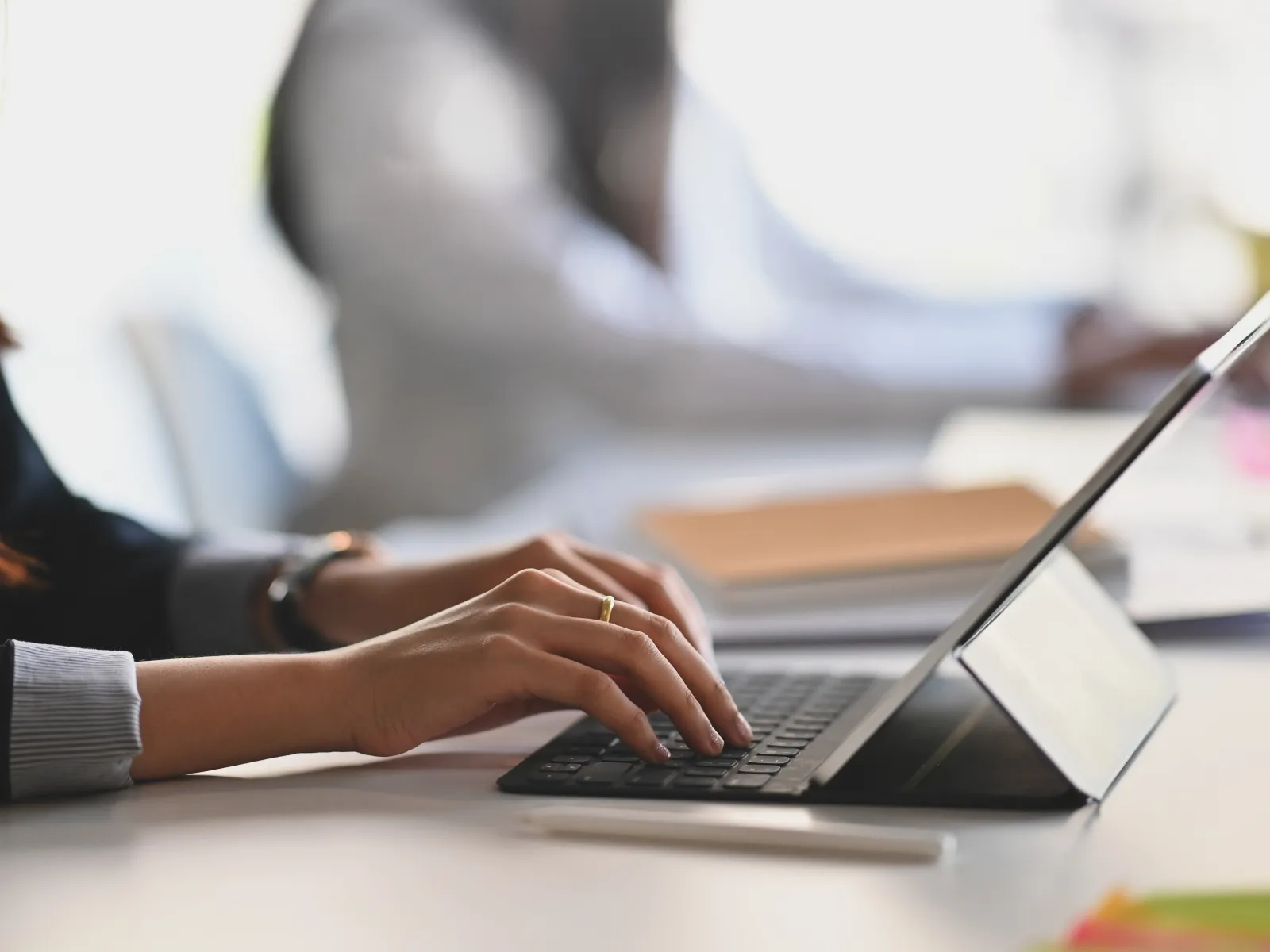 Close-up of a person typing on a tablet keyboard in a modern office setting with blurred background.