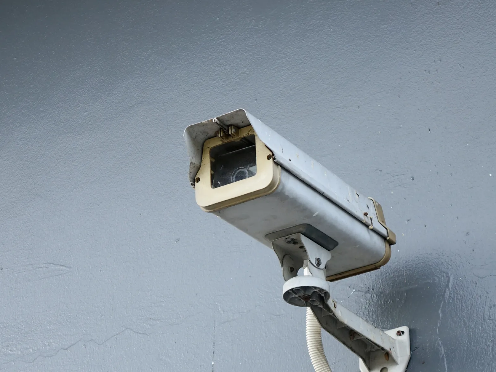 Surveillance camera mounted on a gray wall, monitoring the area for security purposes.