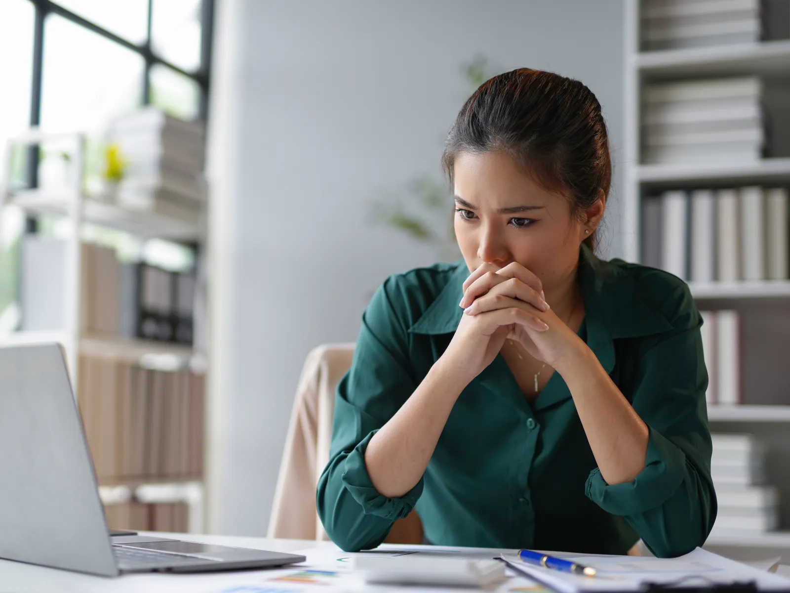 Woman in green shirt intensely focused on laptop screen working at desk in office environment.