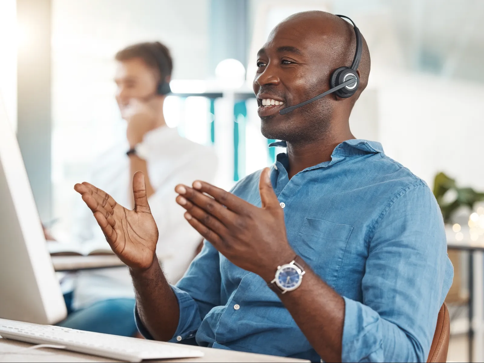 Smiling customer service agent in headset talking and gesturing in a modern office call center.