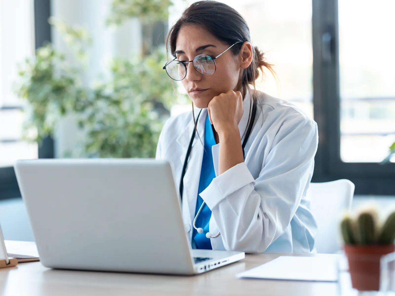 Focused woman working on a laptop in a bright office space with documents on the desk