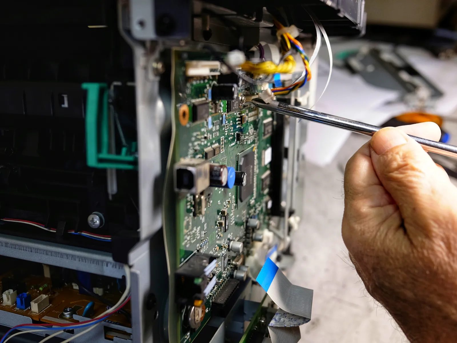 Technician repairing electronic circuit board inside a device using a screwdriver with visible wires and components.