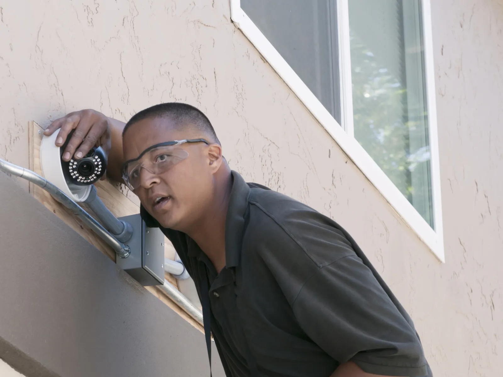 Technician installing a security camera on the exterior of a building using a ladder.