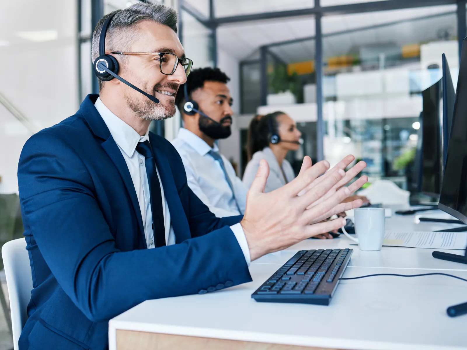 Smiling male customer service representative wearing headset communicating at computer in modern office.