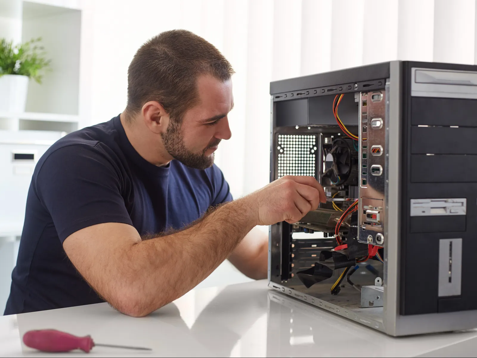 Man repairing or assembling a desktop computer with open case on a white desk in indoor setting