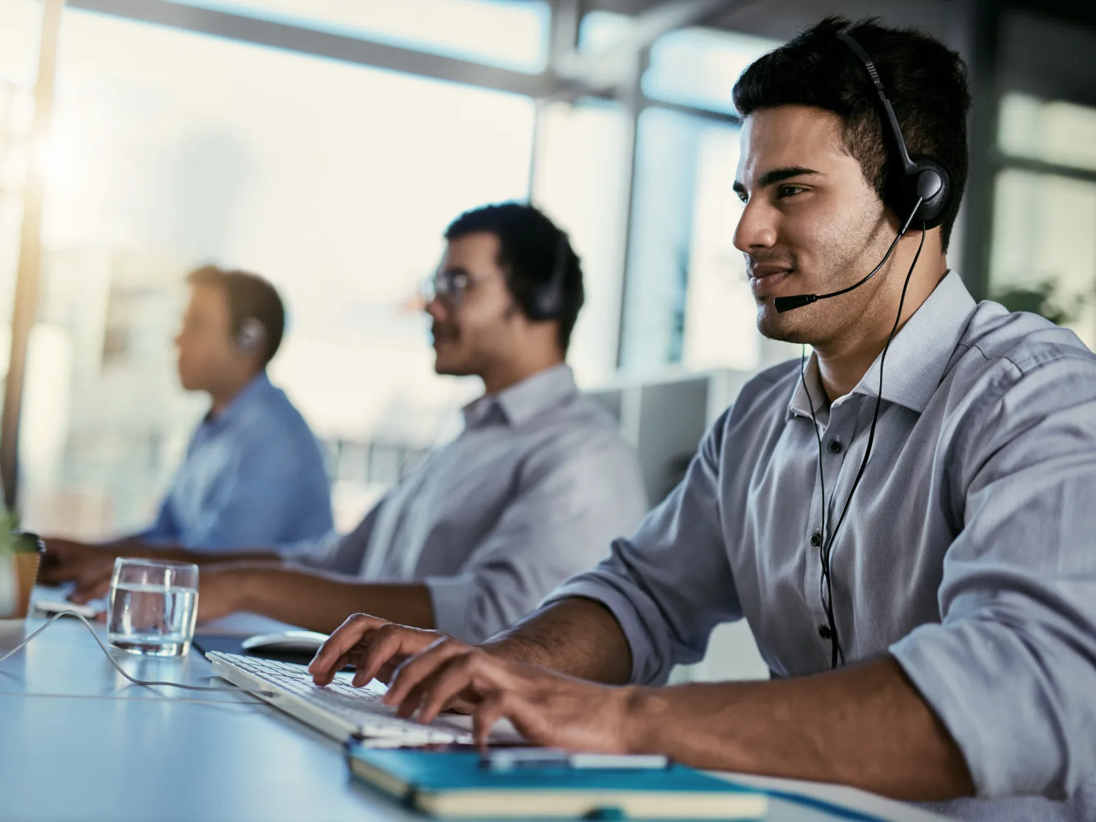 Customer service representatives wearing headsets working at computers in a modern office environment.
