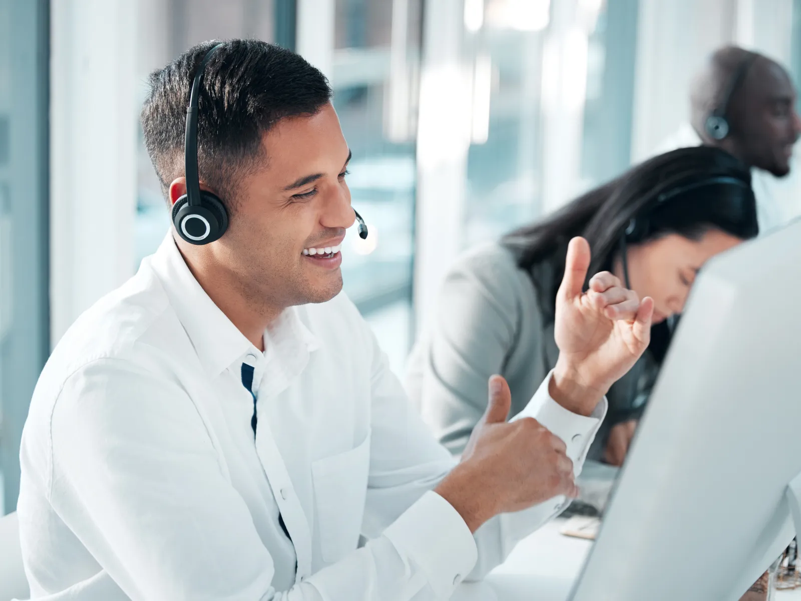 Customer service representative wearing headset smiling and gesturing while working at computer in office.