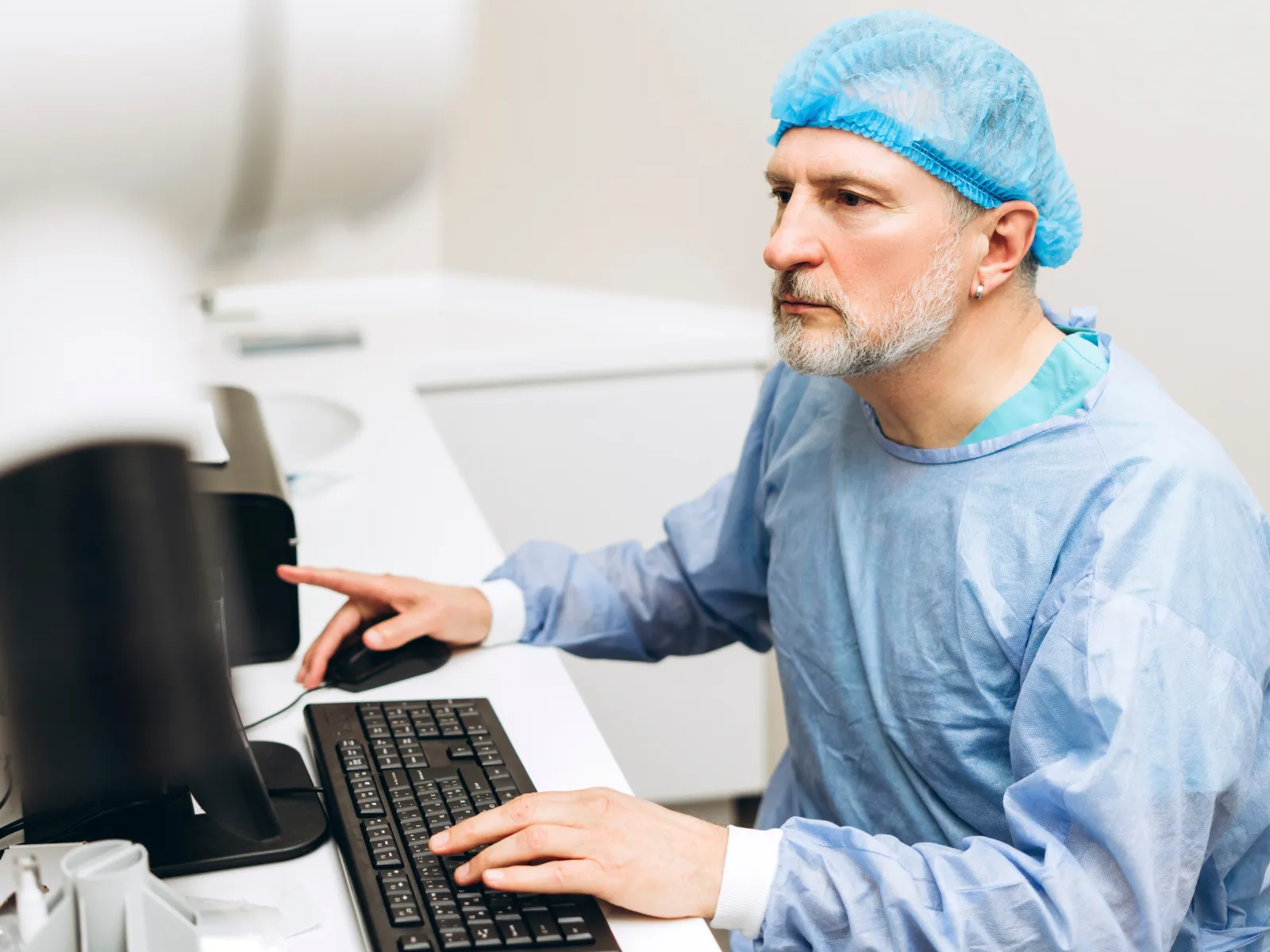 Scientist in blue lab coat and hairnet using computer in laboratory environment