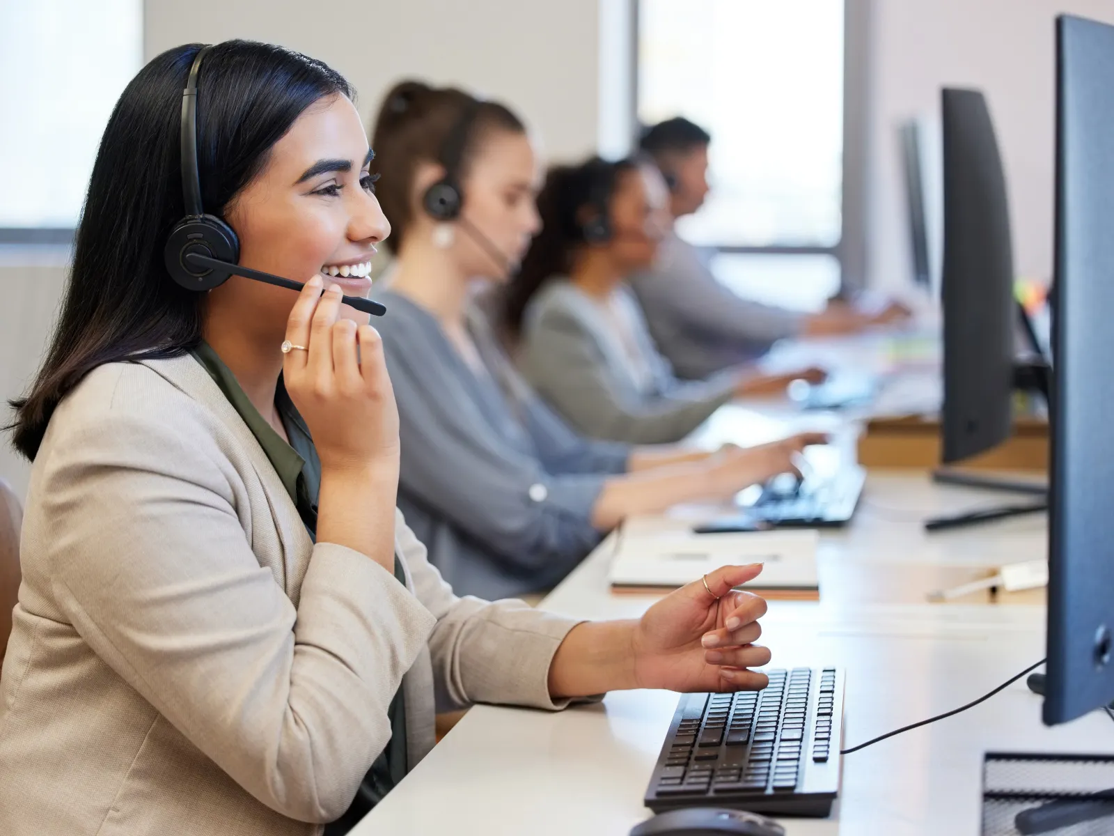 Customer service team in office wearing headsets and working on computers with focus on smiling woman.