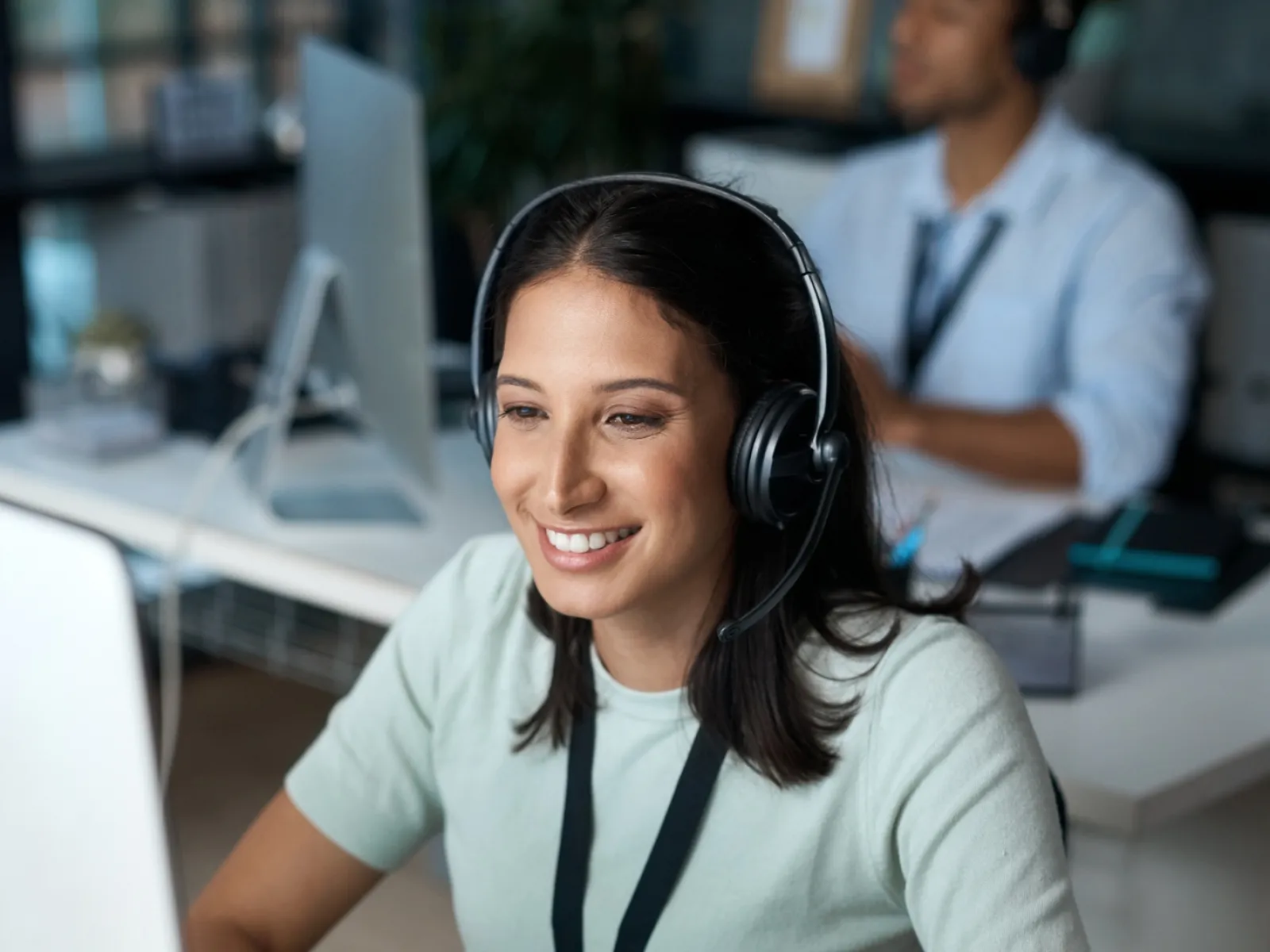 Young woman working at desk with headset, focused on computer screen, in a modern office setting.