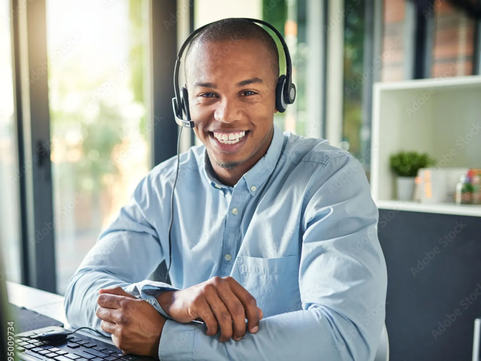 Smiling man in headset working at computer in modern bright office environment