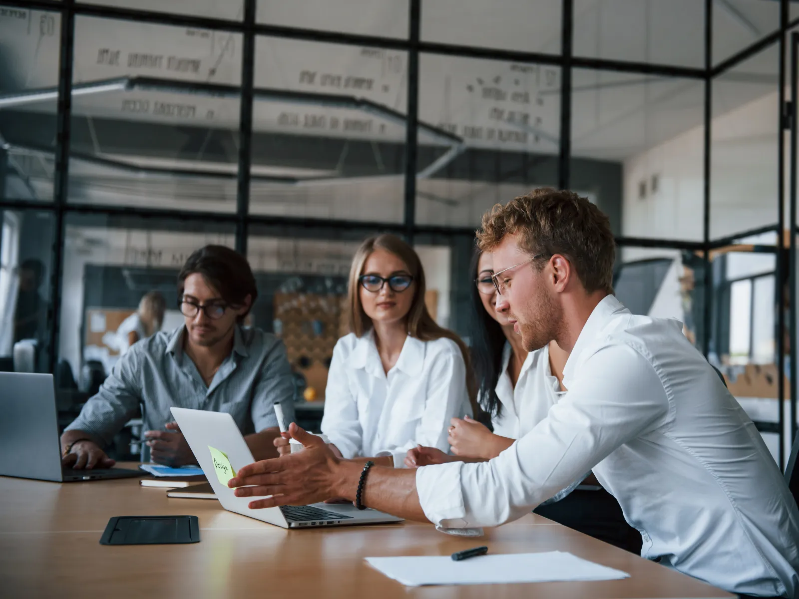 Team of young professionals collaborating on laptops around a conference table in a modern office.