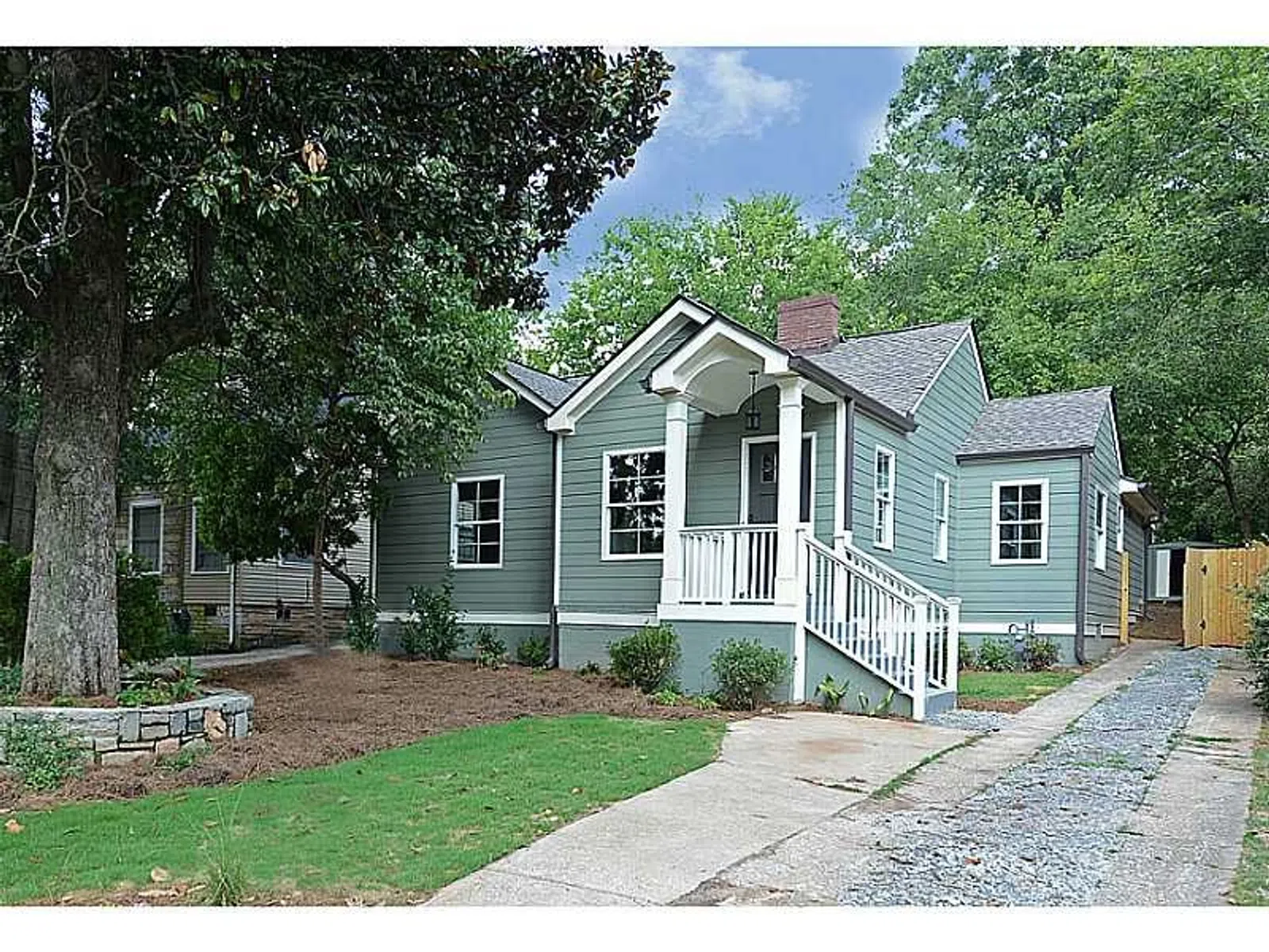 Charming single-story gray house with white trim, front porch, greenery, and a driveway leading to a backyard gate.