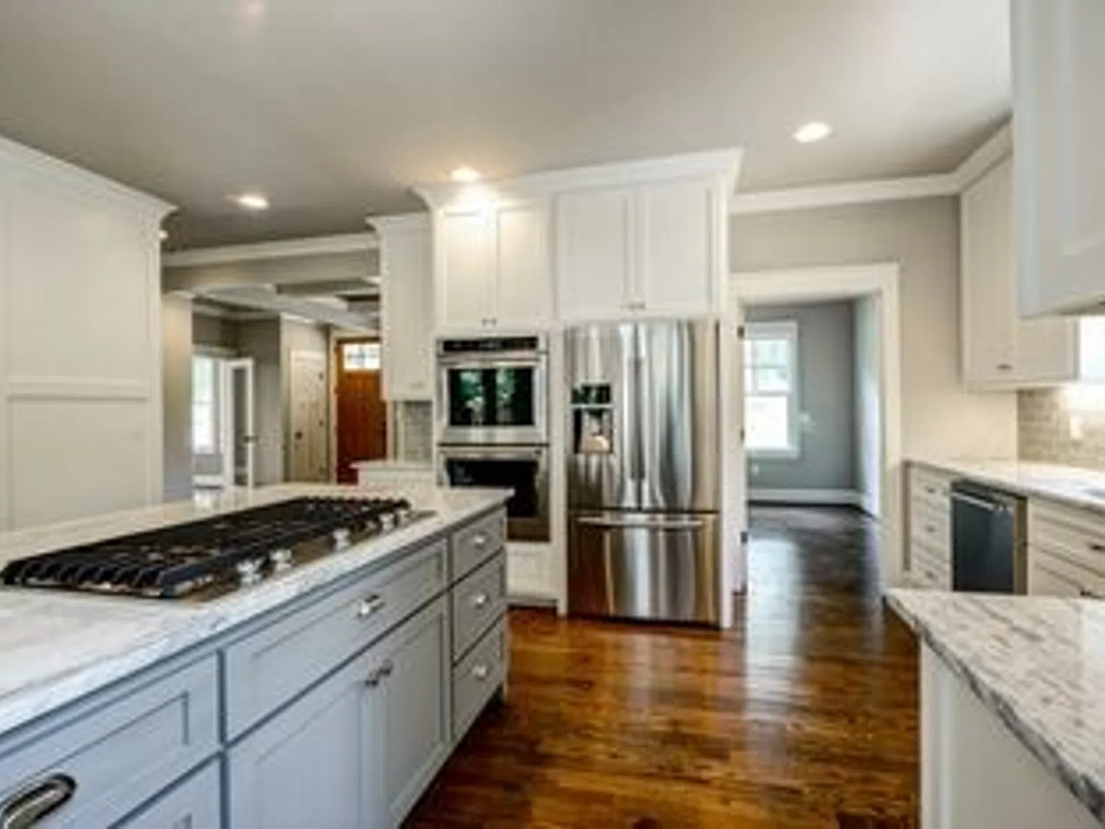 Modern kitchen with gray island, white cabinets, stainless steel appliances, and hardwood flooring in open layout