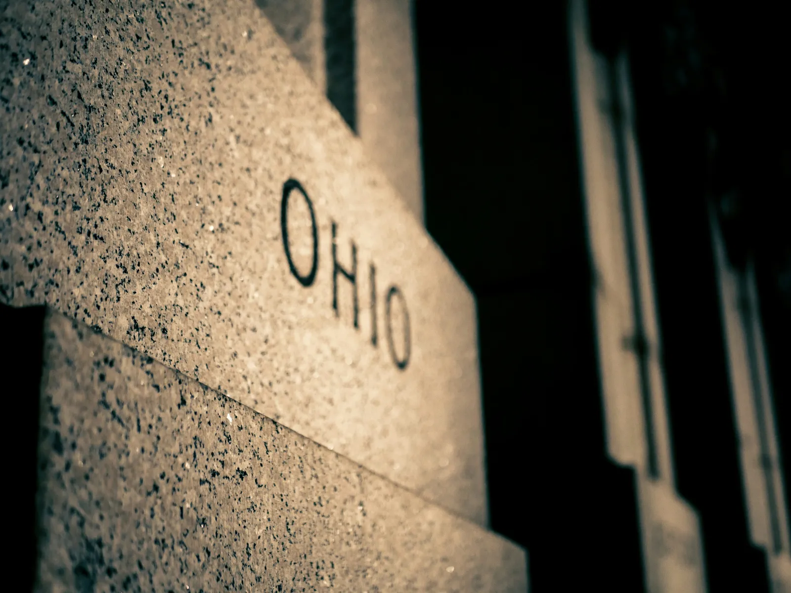 Close-up of a granite wall with the word OHIO engraved, highlighting texture and shadows in low light.