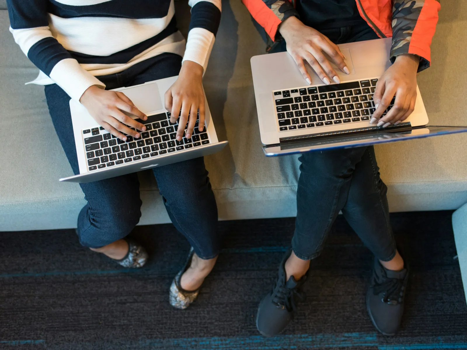a couple of people sitting on a bench with laptops