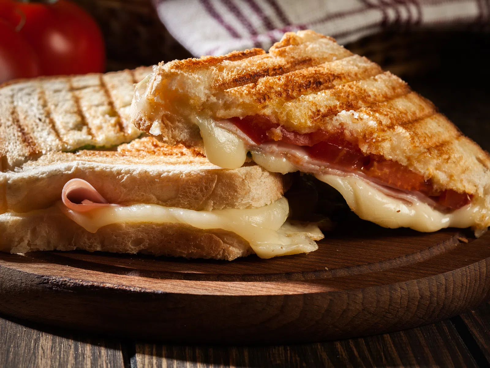 Grilled ham and cheese sandwich with melted cheese and tomato slices on wooden board