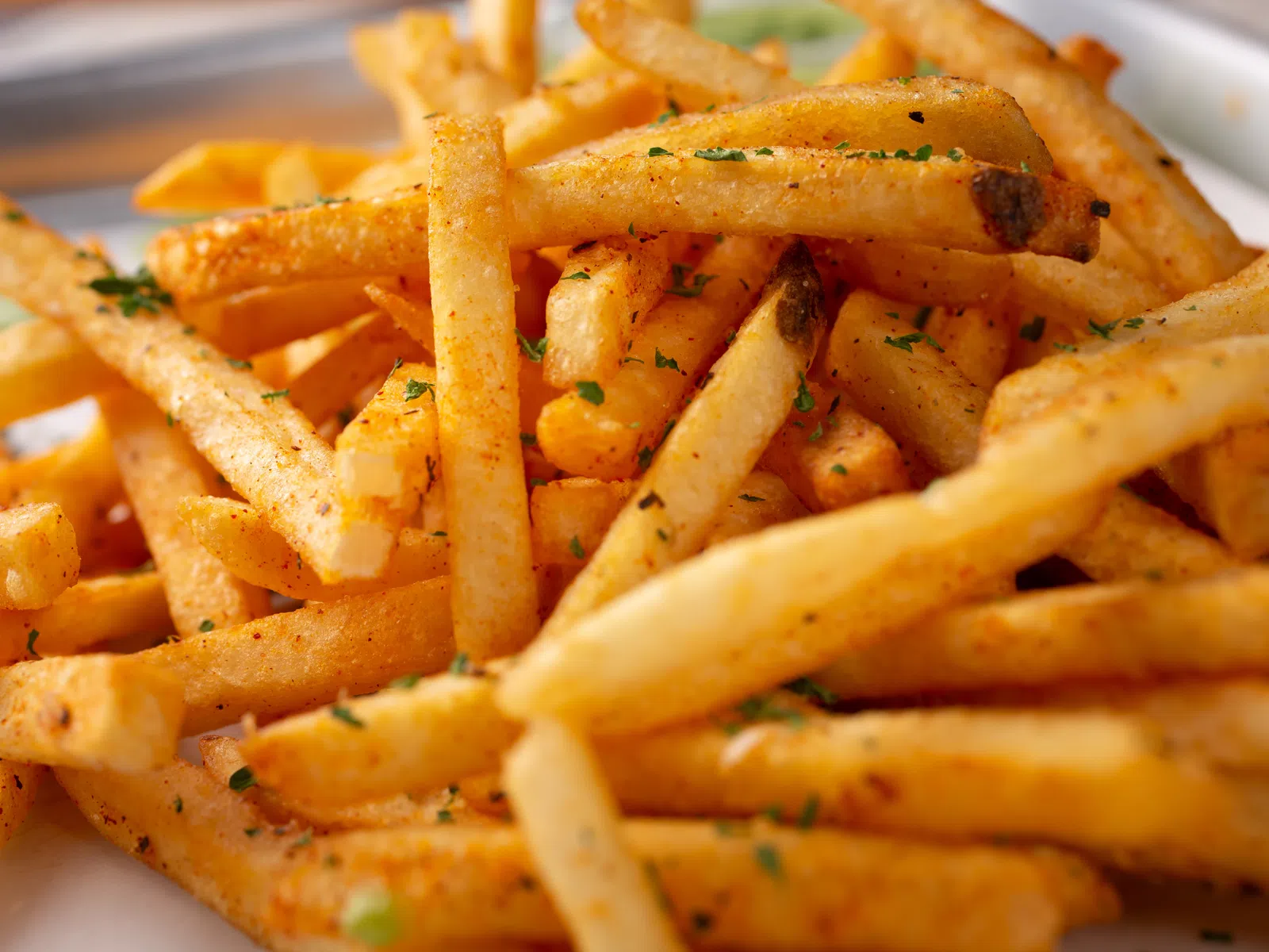 Crispy seasoned French fries garnished with herbs served on a white plate.