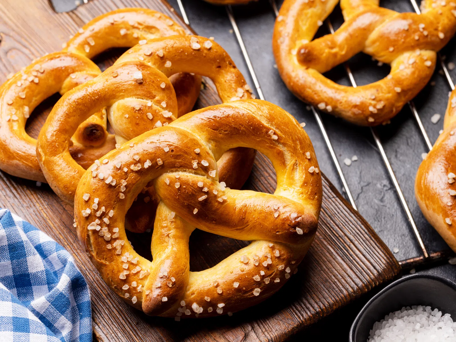 Freshly baked soft pretzels sprinkled with coarse salt on a wooden board and cooling rack.