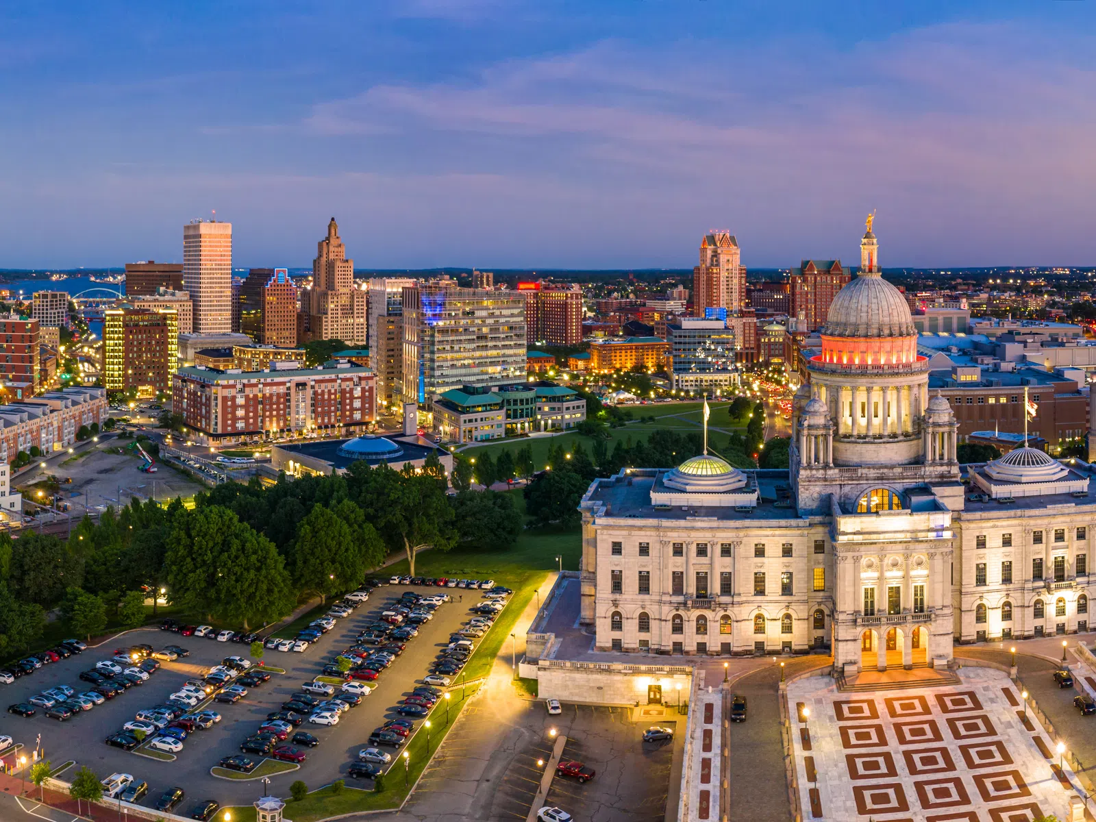 Aerial view of a cityscape at dusk with a lit historic capitol building and surrounding urban skyline.