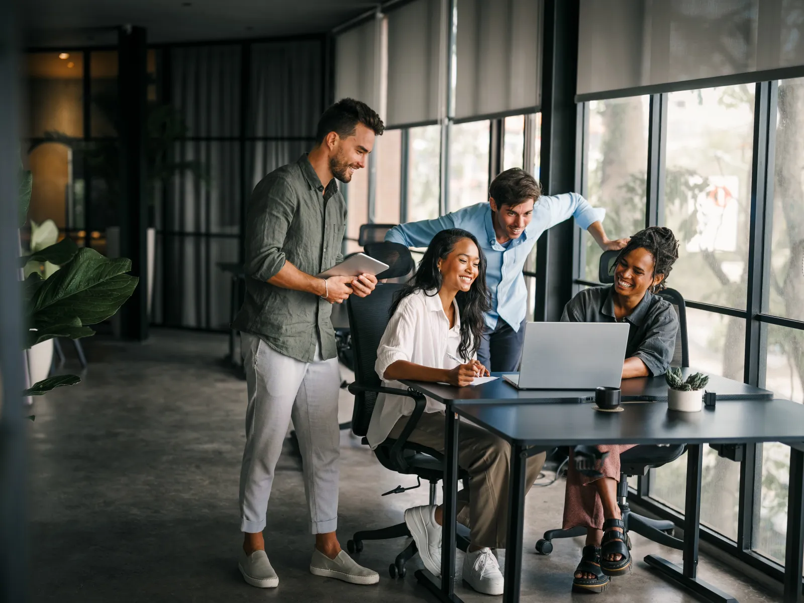 Diverse young professionals collaborating happily around a laptop in a bright modern office workspace.