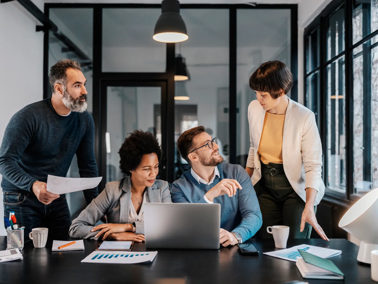 Four diverse professionals collaborating in a modern office around a laptop and documents during a meeting.