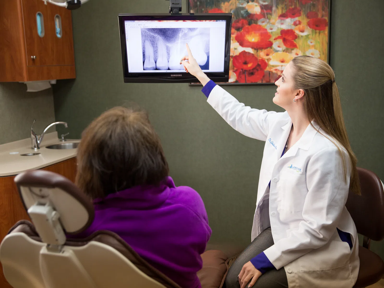 Dentist explaining dental X-ray results to patient in a modern dental office with colorful artwork.