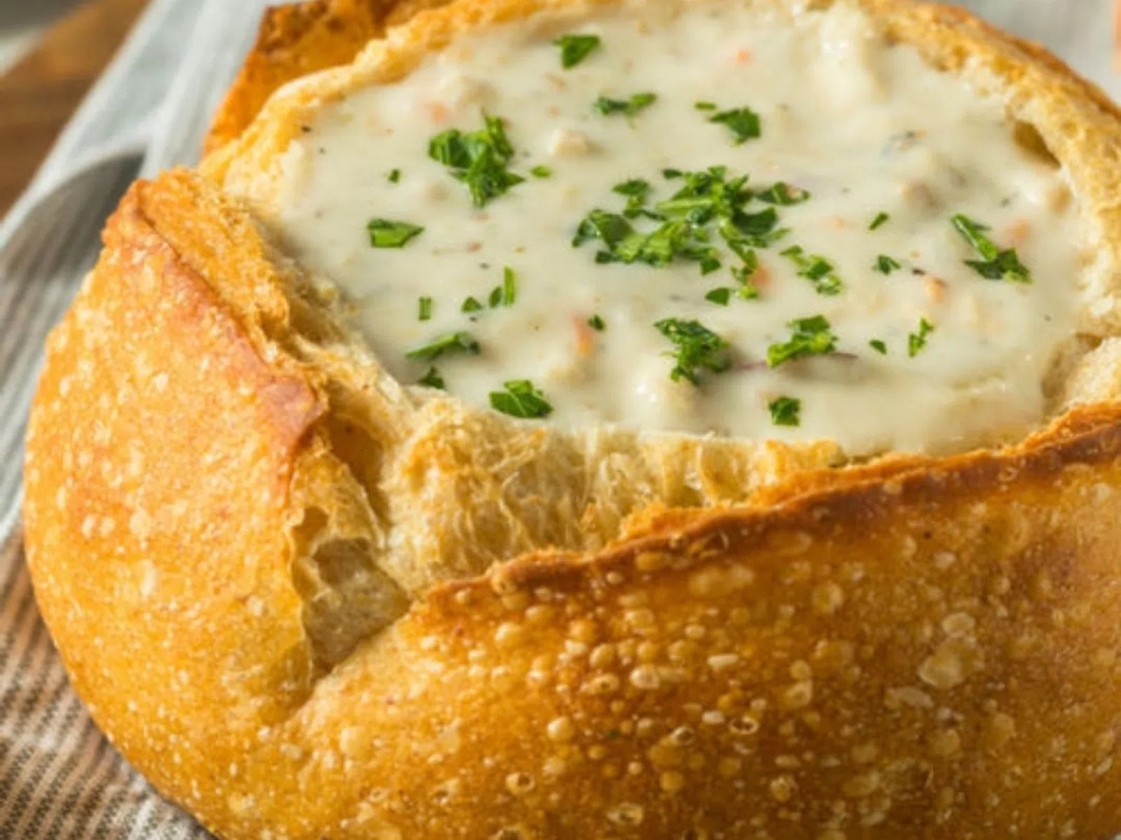 Creamy clam chowder served in a crusty bread bowl garnished with chopped parsley.