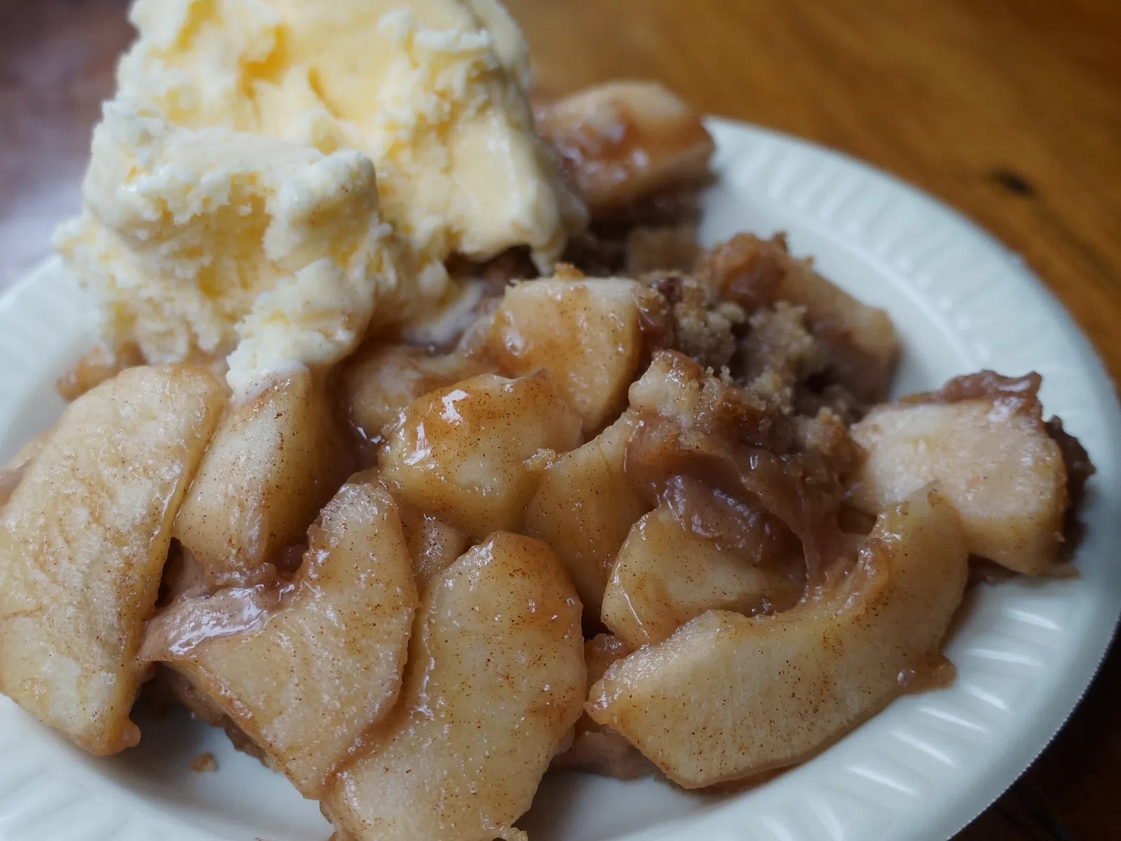 Warm cinnamon apple crisp dessert served with a scoop of vanilla ice cream on a white plate.