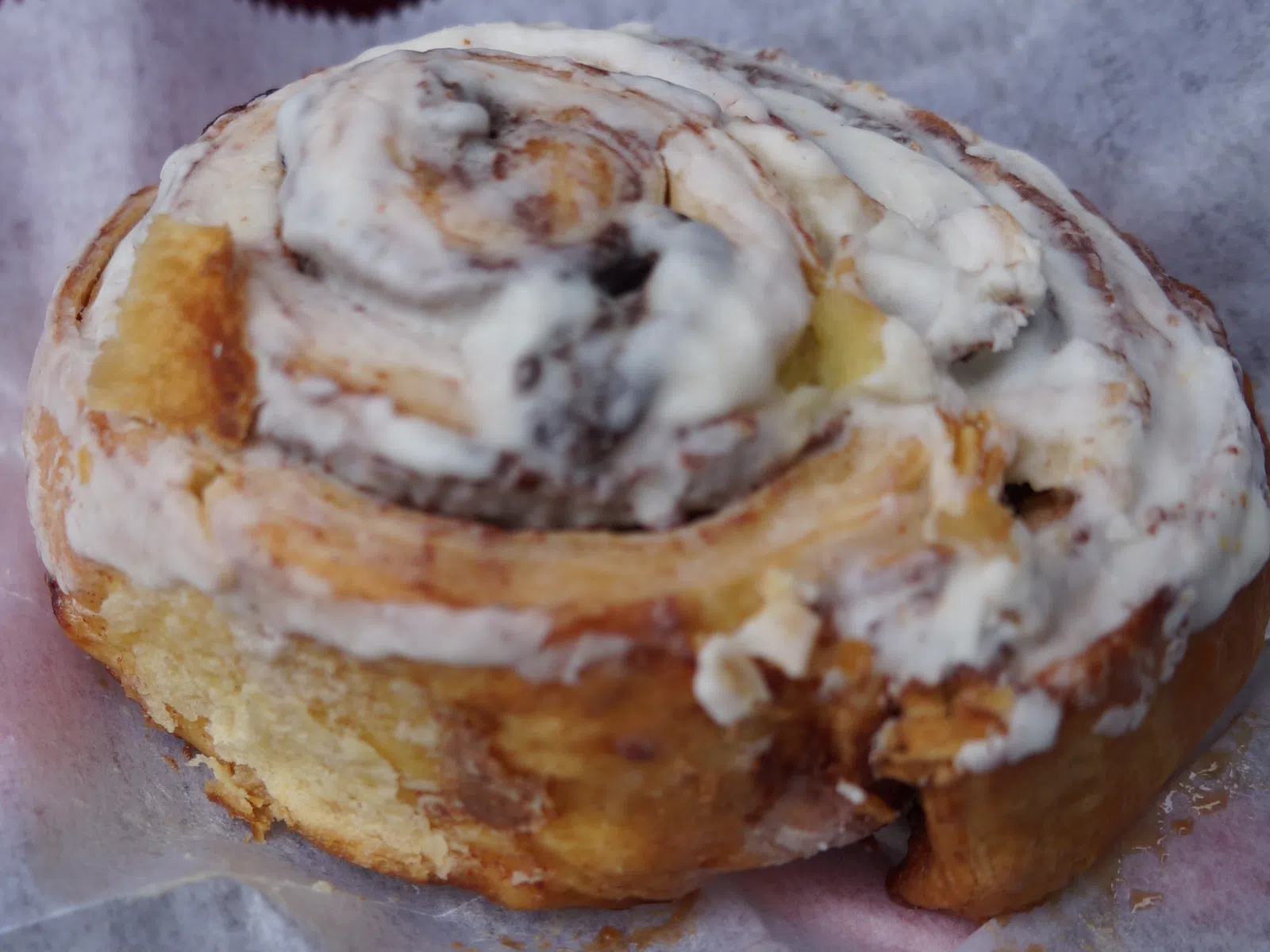 Close-up of a freshly baked cinnamon roll with creamy white icing on parchment paper.