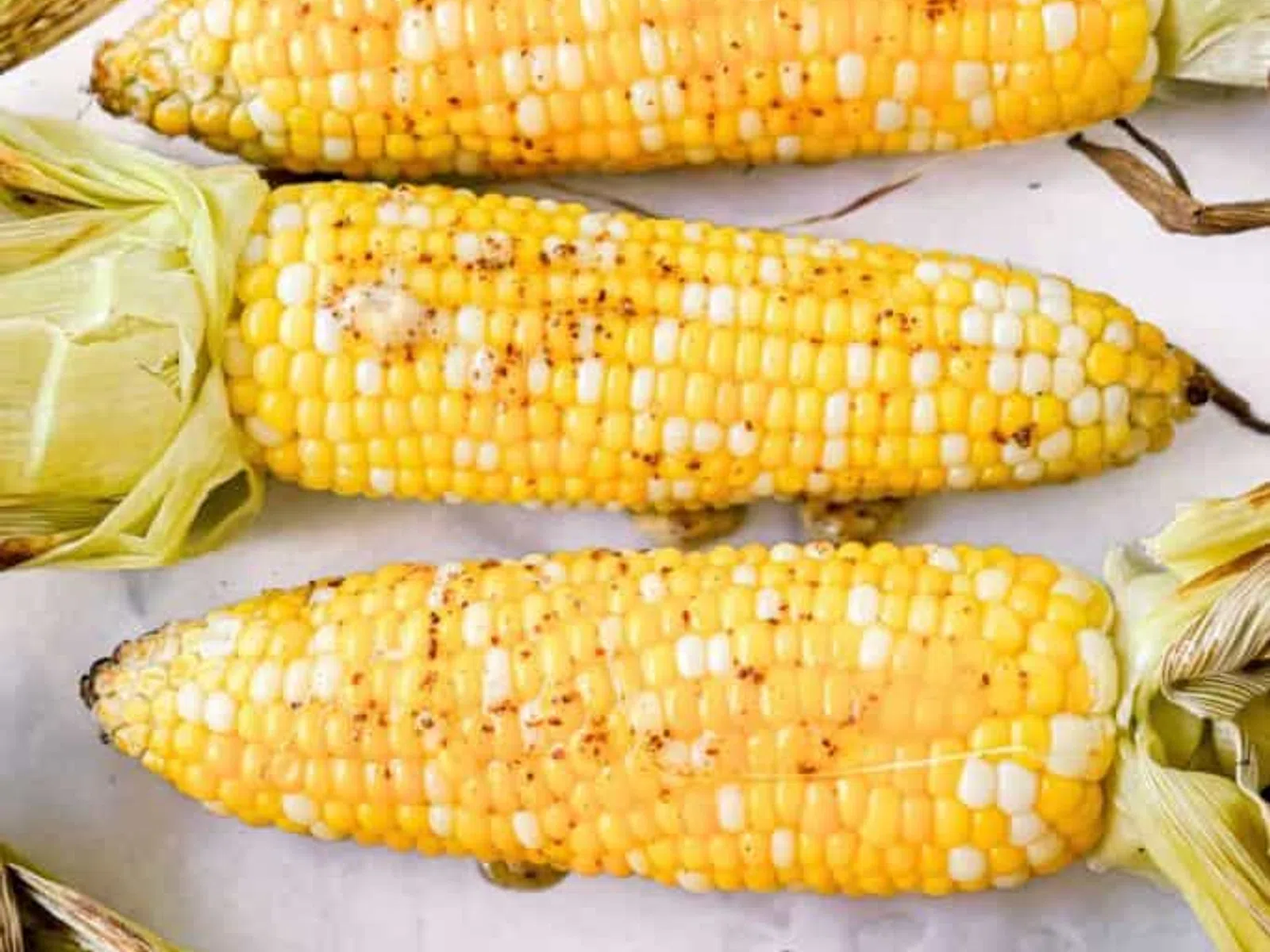 Five ears of corn with husks partially removed